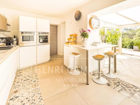 Cuisine moderne et lumineuse d'une villa contemporaine avec bar et accès à un jardin.