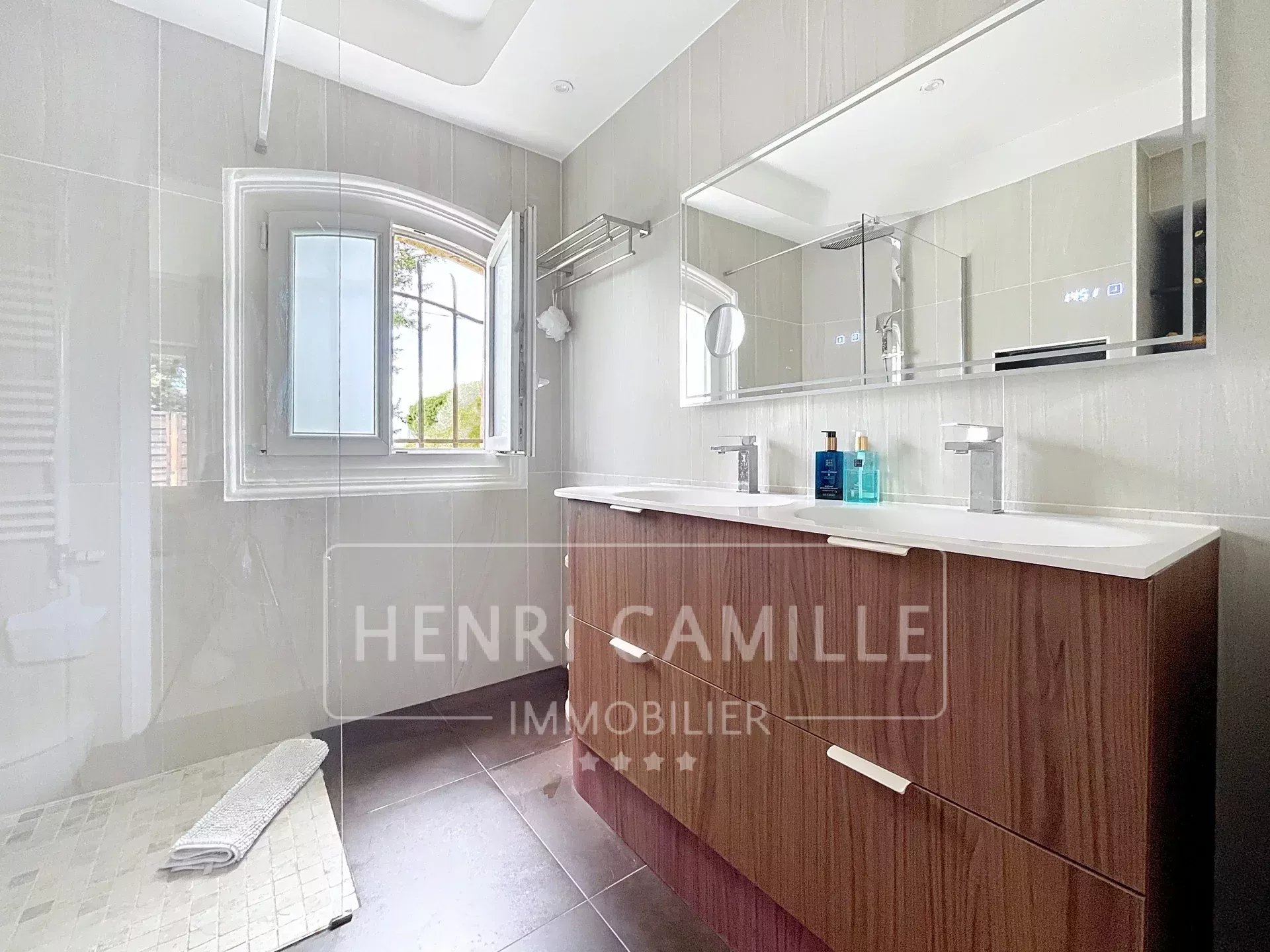 Salle de bain moderne avec meuble en bois et double vasque, fenêtre ouverte.