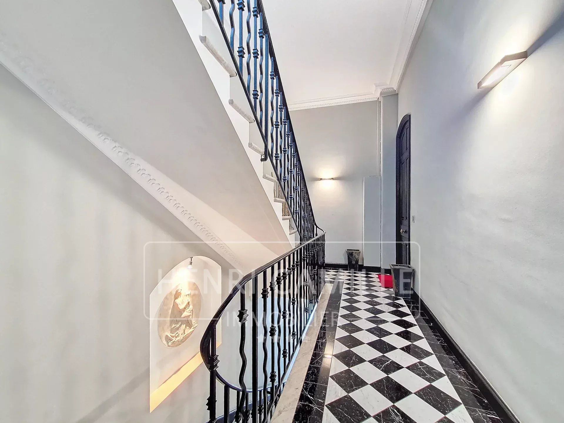 Staircase of a private mansion in Cannes with a black and white checkered floor and wrought iron balustrade.