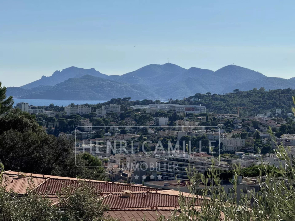 Vue dégagée sur la mer et les montagnes depuis Le Cannet, avec des bâtiments en arrière-plan.