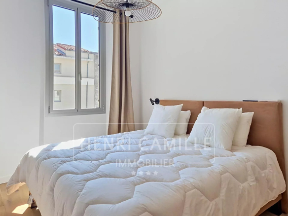 Chambre d'un appartement rénové à Cannes, avec lit double et fenêtre laissant entrer la lumière.