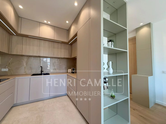 Cuisine moderne et équipée d'un appartement rénové à Cannes, avec meubles en bois et plan de travail clair.