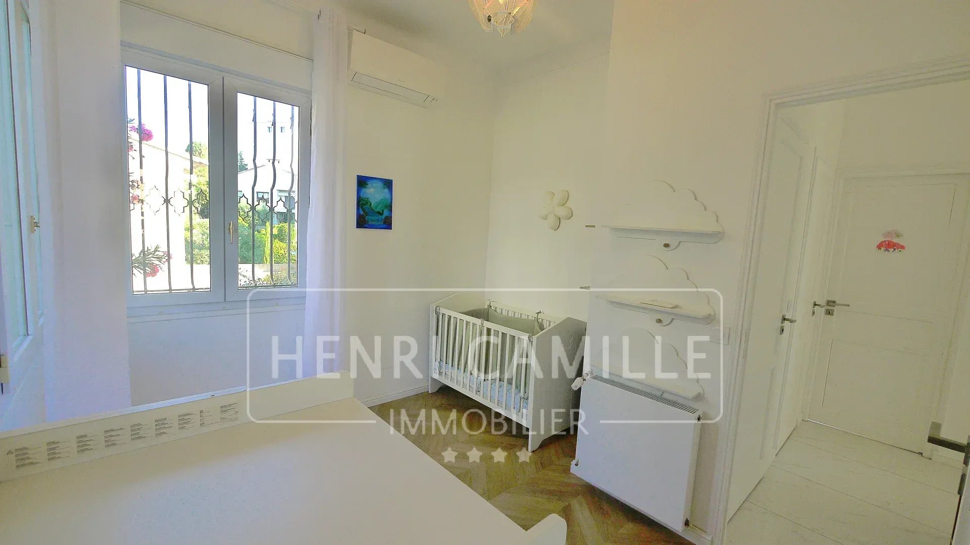 Bright room with a baby cot and storage furniture, windows overlooking the outside.