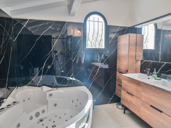 Luxurious bathroom with a white corner whirlpool tub, black veined marble walls, and a wooden double-sink vanity.