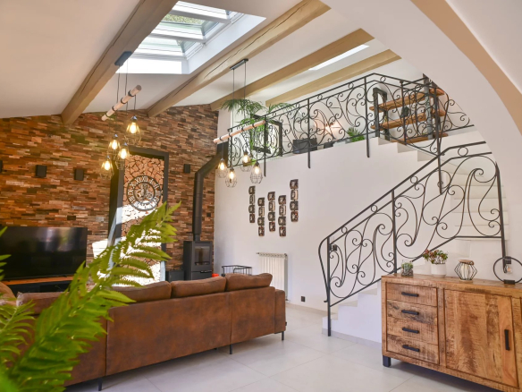 Living room with brown leather sofa, brick accent wall, a large wall clock, and a decorative black wrought-iron staircase railing.