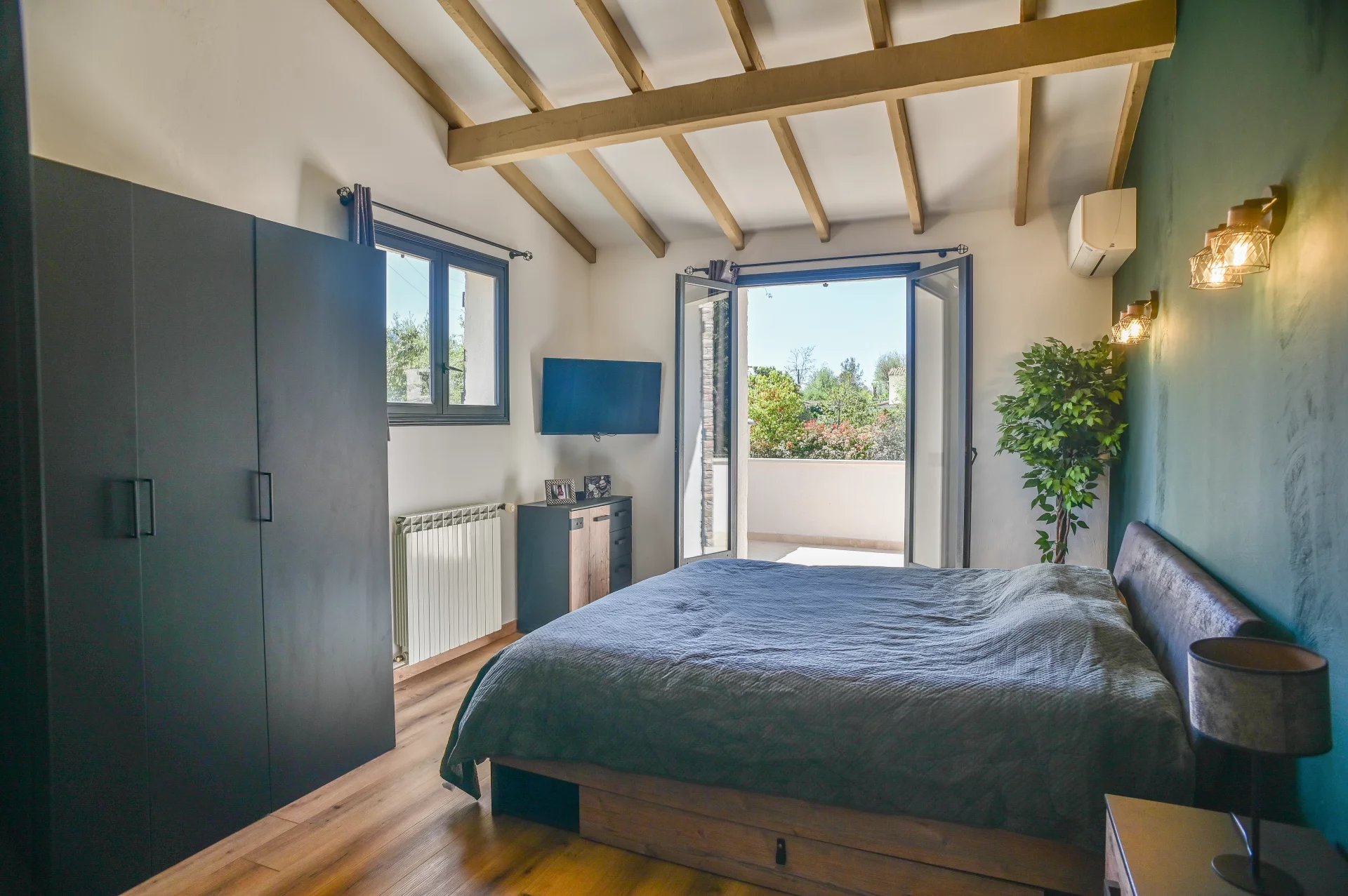 Bedroom with dark green feature wall, exposed wooden beams, and a low platform bed facing a balcony door.