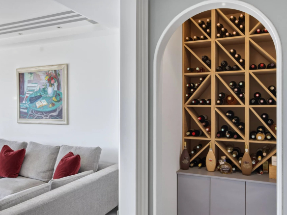 Modern living room with a gray sectional sofa, red throw pillows, and a framed colorful painting on a white wall.