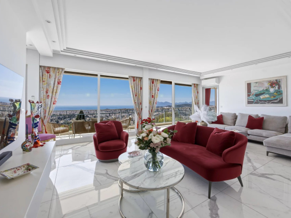 Bright living room with white marble floors, a red velvet sofa and chairs, and a panoramic ocean view through large windows.