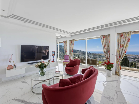 Bright living room with red velvet lounge chairs, marble floor, and a sea-view balcony through large windows.
