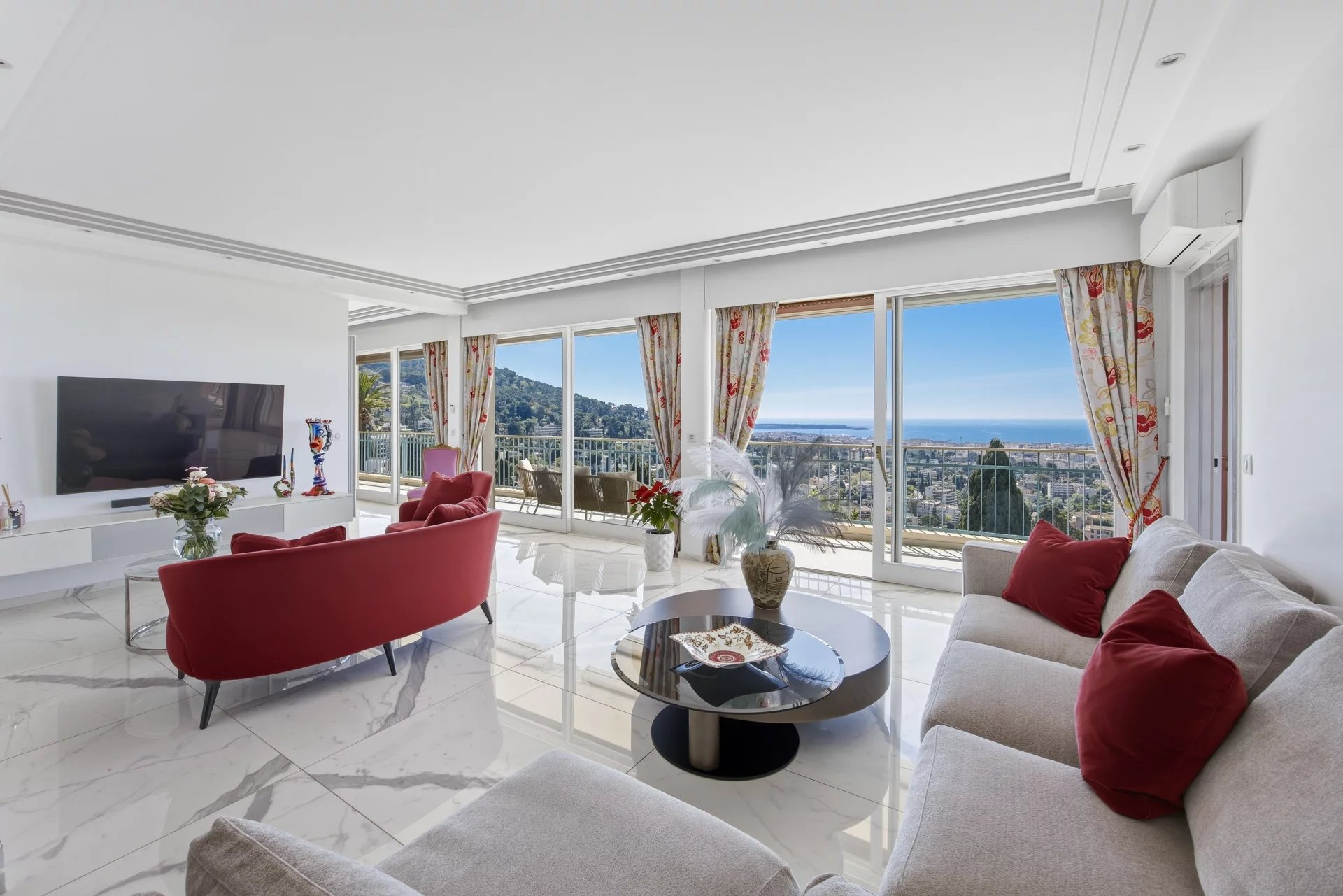 Bright living room with marble floors, red sofa and chairs, and large windows showing an ocean view.