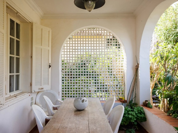 Terrace of a villa with a wooden table and white chairs, surrounded by greenery.