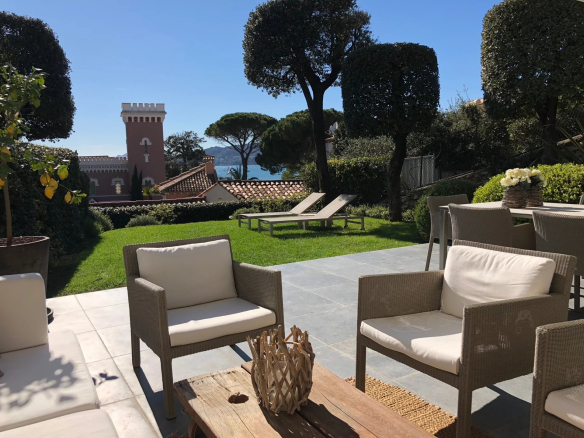 Terrasse d'un appartement avec vue sur la mer, chaises et transats dans un jardin bien entretenu à Antibes.