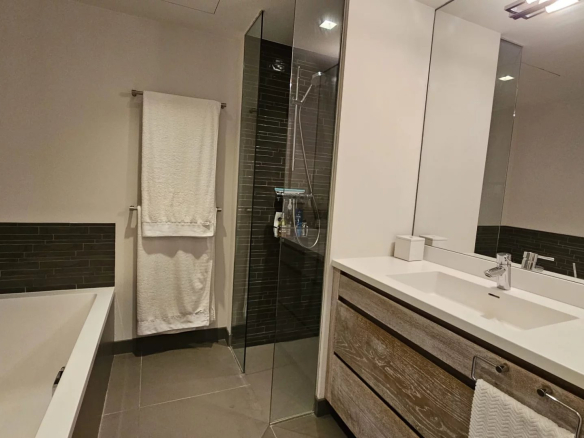 Modern bathroom with bathtub and shower, tiled walls and wooden vanity unit.