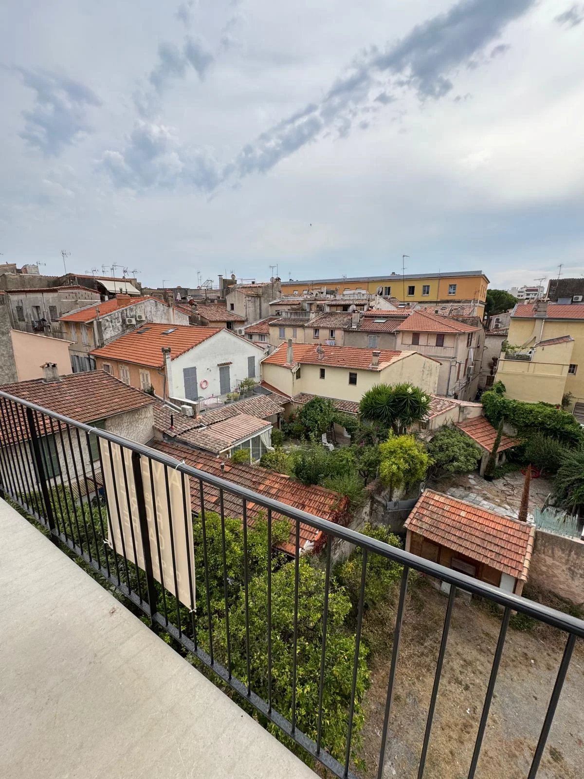Vue depuis le balcon d'un appartement au vieux Antibes, montrant des toits de maisons et des jardins.