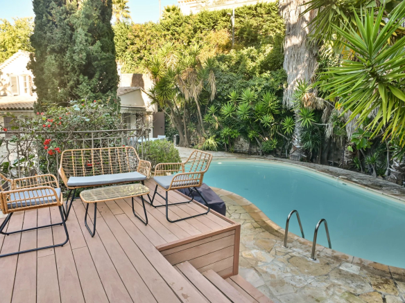Piscine entourée de verdure et de chaises en osier dans un jardin à Cannes.