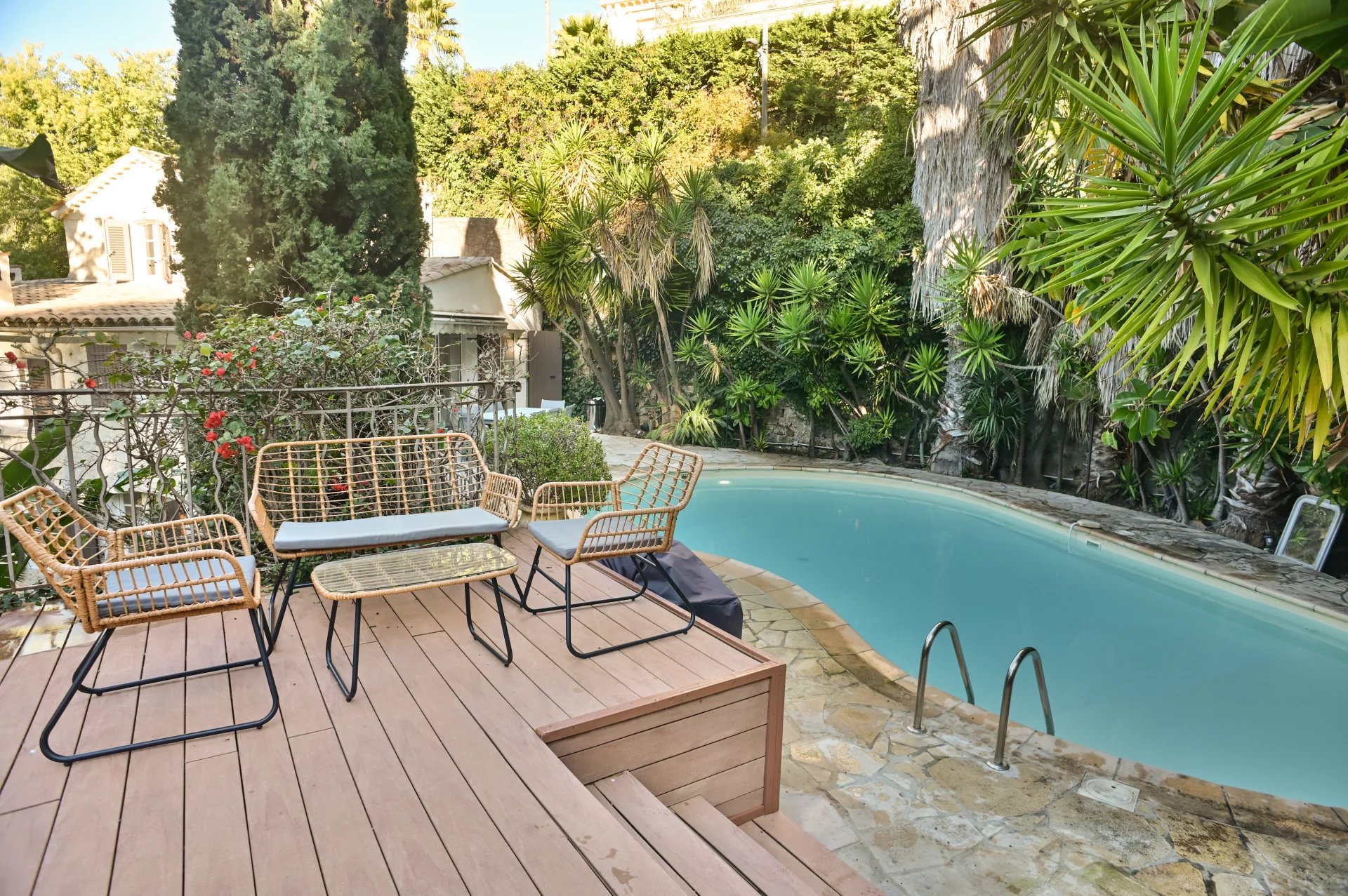 Piscine entourée de verdure et de chaises en osier dans un jardin à Cannes.
