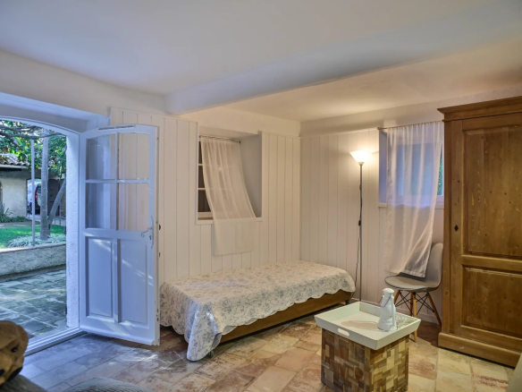 Intérieur d'une chambre avec un lit, une fenêtre ouverte sur le jardin et un meuble en bois.