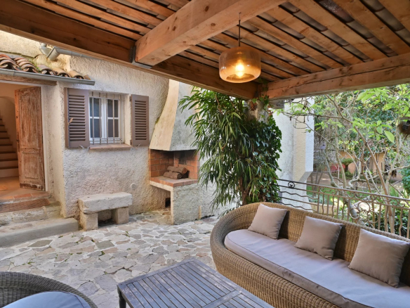 Terrasse d'une propriété rénovée avec un coin salon et un barbecue, entourée de verdure.