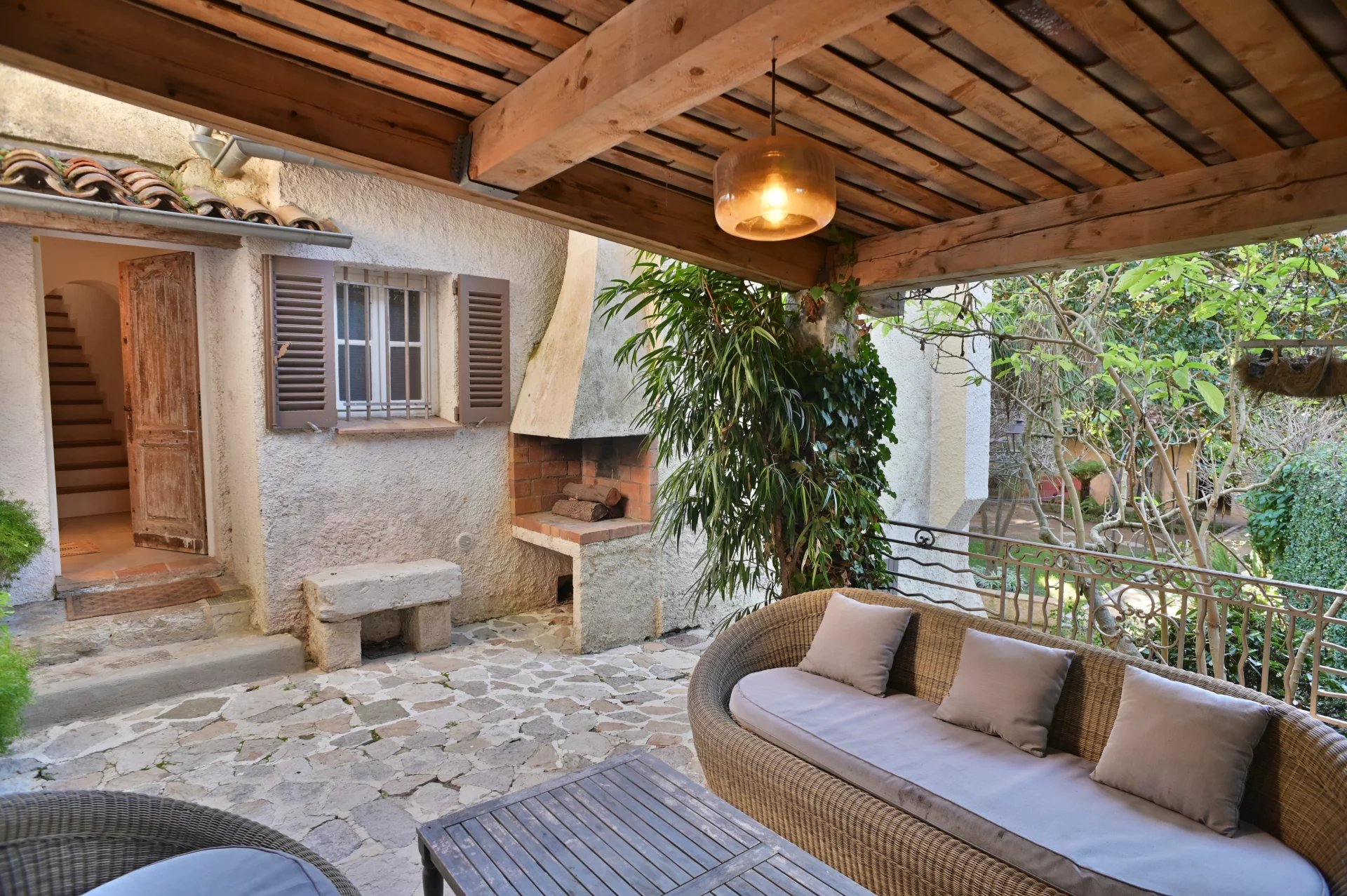 Terrasse d'une propriété rénovée avec un coin salon et un barbecue, entourée de verdure.