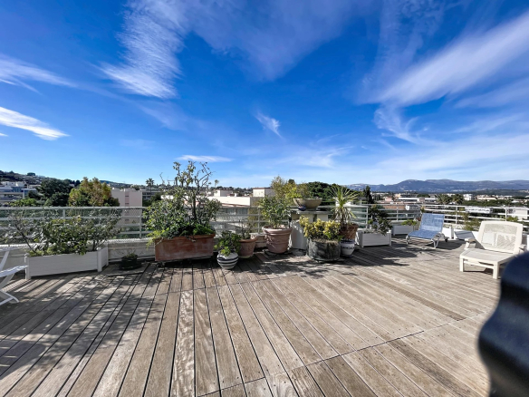 Terrasse spacieuse avec vue sur la mer et les montagnes à Antibes, ensoleillée et entourée de plantes.