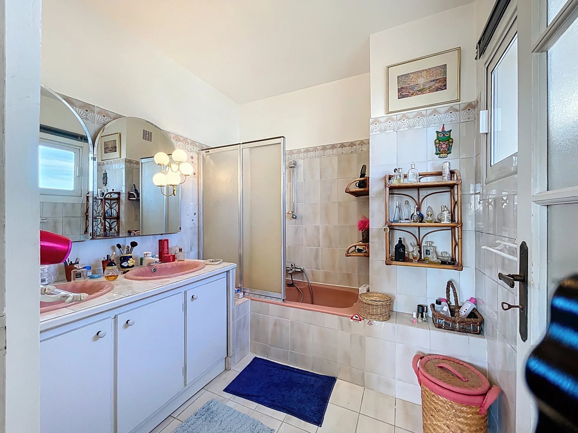 Salle de bain d’un appartement à Antibes Salle de bain spacieuse avec baignoire, double vasque et miroir, décorée de carrelage clair.