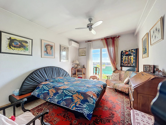 Chambre d'un appartement à Antibes avec lit, fauteuils et vue sur la mer.