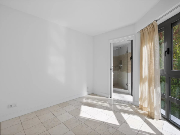 Interior of a bright apartment with tiled floor and windows opening to the outside.