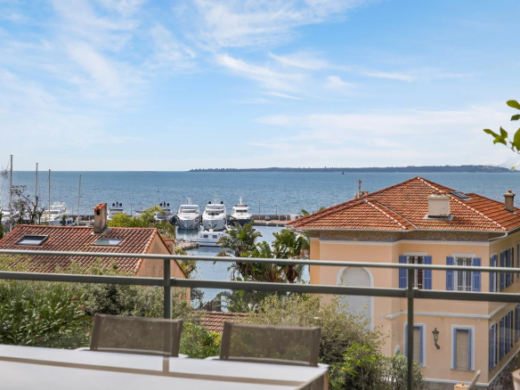 Panoramic sea view from a terrace, with yachts in the port and houses in the background.