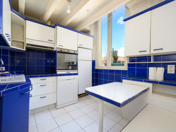 Kitchen of a 3-room apartment in Cannes with blue and white tiles, bright windows.