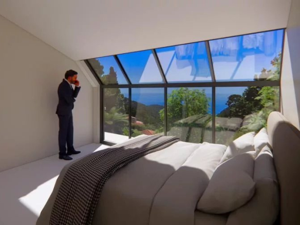 Chambre moderne avec vue sur la mer et grandes fenêtres, homme en costume debout près de la fenêtre.