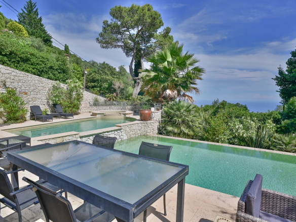 Vue sur la piscine et le jardin d'une villa à Eze, avec mer en arrière-plan.