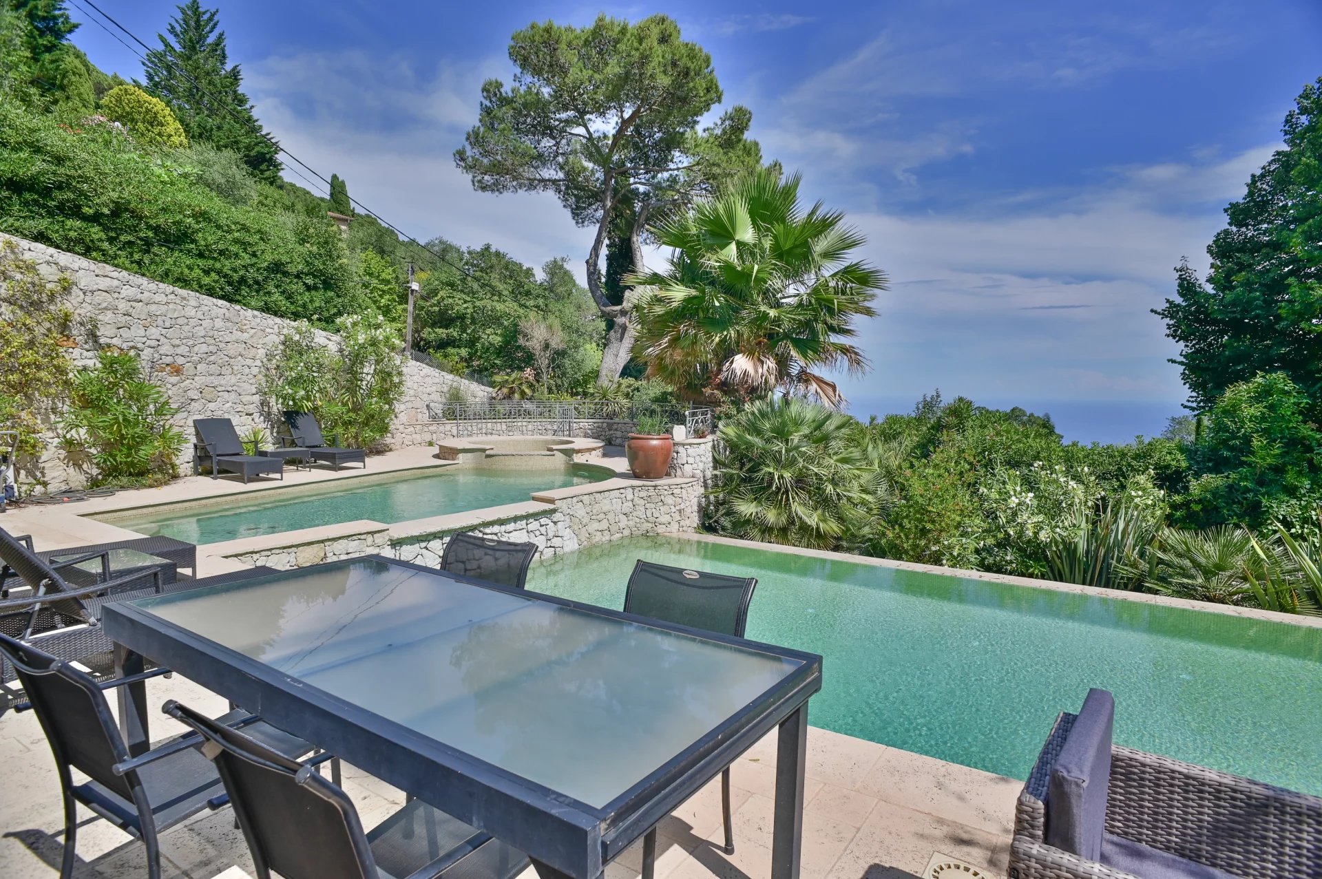 Vue sur la piscine et le jardin d'une villa à Eze, avec mer en arrière-plan.