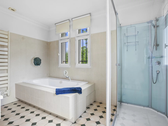 Salle de bain spacieuse avec baignoire et douche, fenêtres laissant entrer la lumière naturelle.