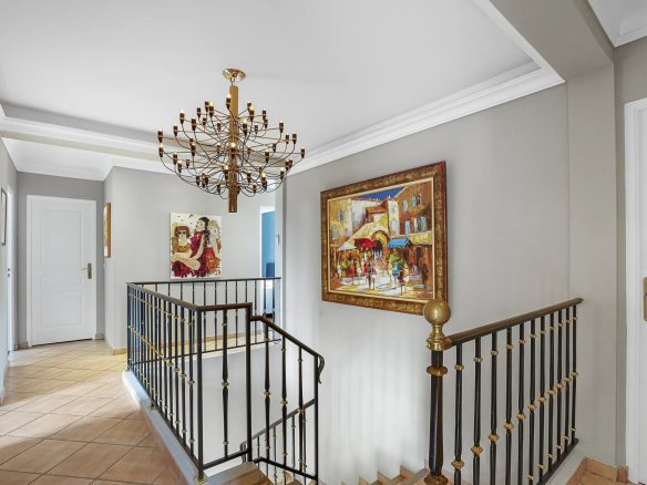 Intérieur d'une villa avec un escalier et un lustre, décoré de tableaux.