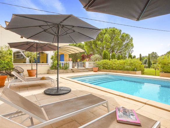 Terrasse avec chaises longues et parasols autour d'une piscine, entourée de verdure.