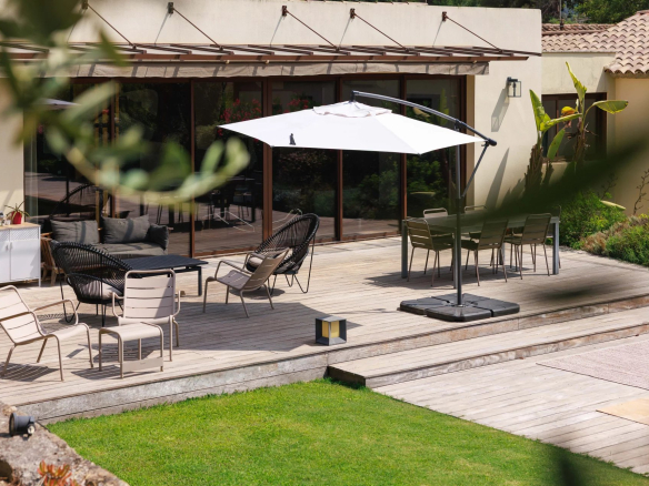 Terrasse en bois avec mobilier moderne et parasol, entourée de verdure dans une bastide rénovée.