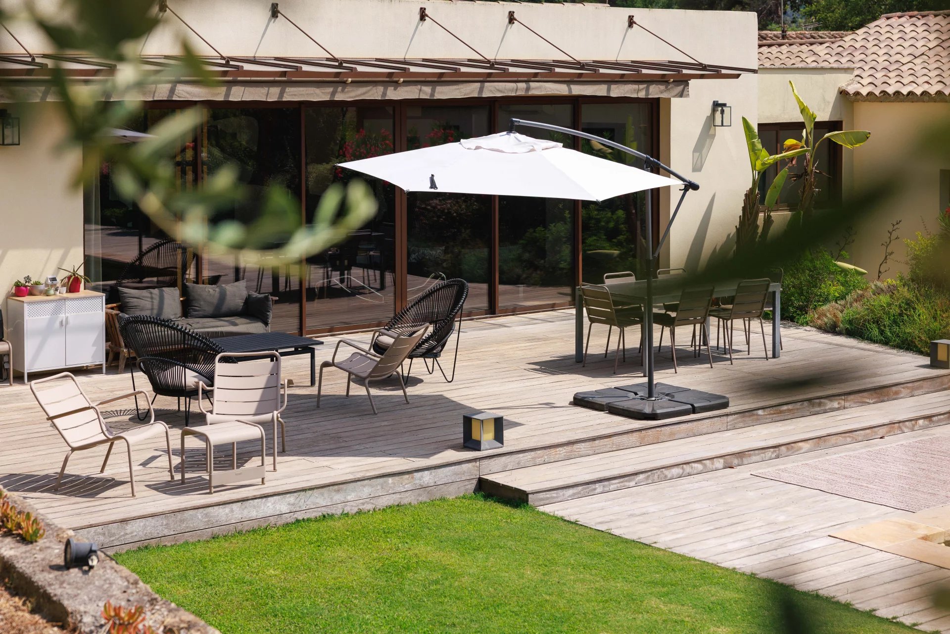 Terrasse d’une bastide rénovée à Mougins Terrasse en bois avec mobilier moderne et parasol, entourée de verdure dans une bastide rénovée.