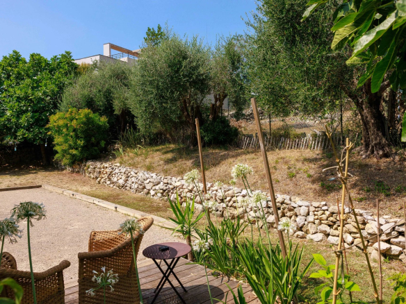 Jardin paysager d'une bastide rénovée avec des chaises en osier et des plantes.