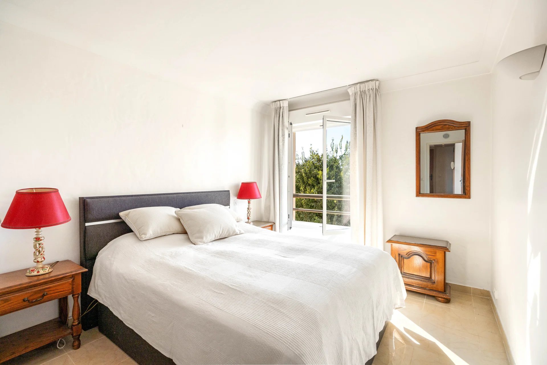 Chambre d'un appartement avec lit double, lampes de chevet et balcon à Antibes.