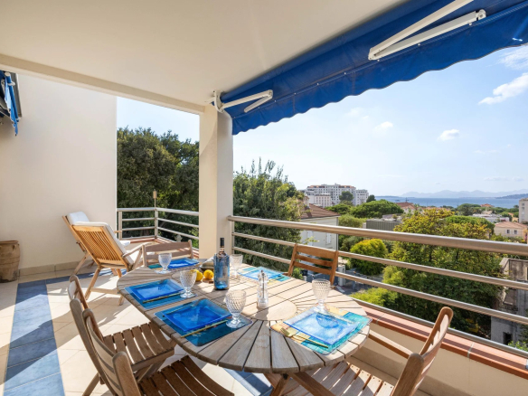 Terrasse d'un appartement avec vue panoramique sur la mer, mobilier de jardin et table dressée.