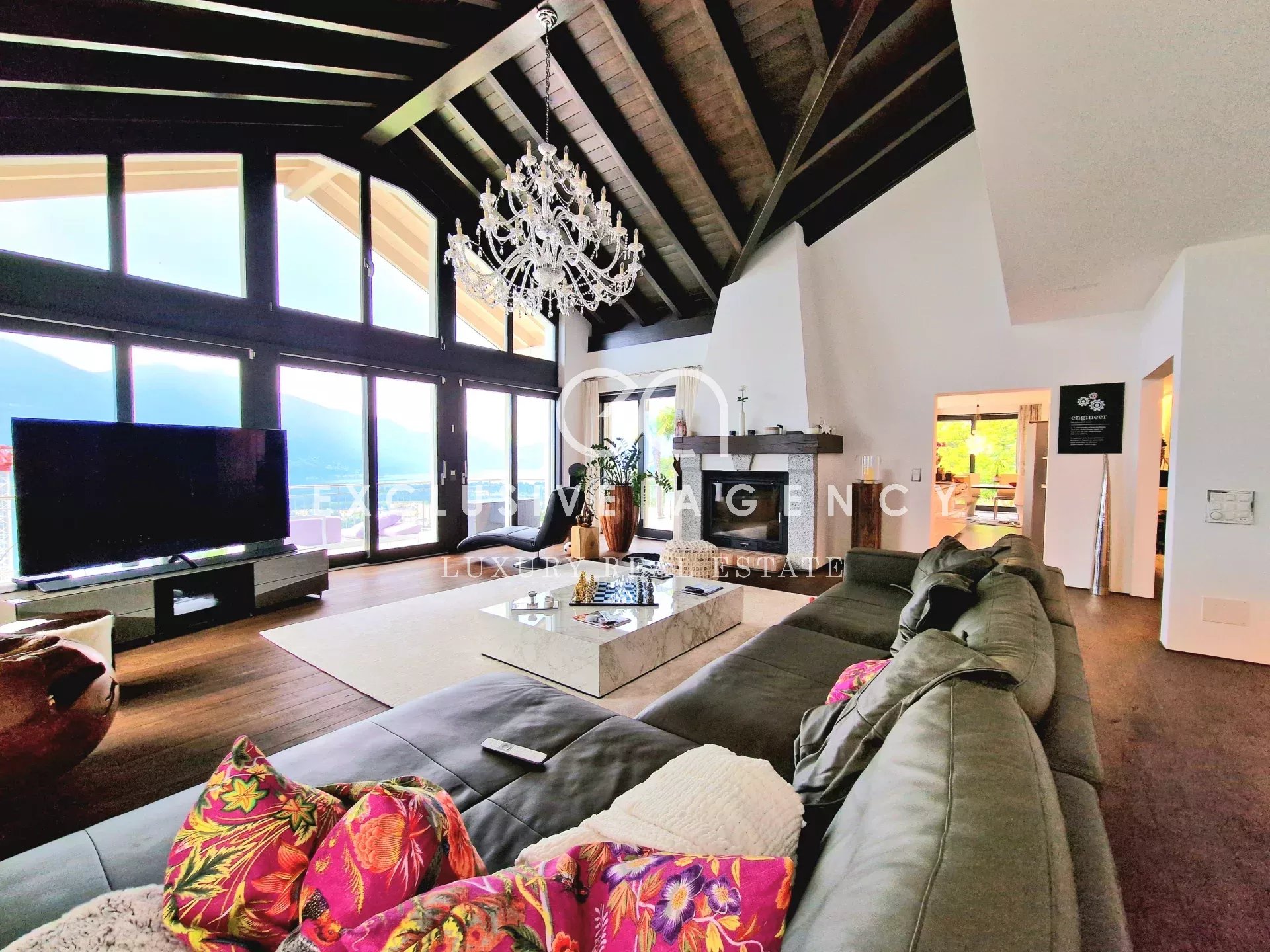 Luxurious open-plan living room with floor-to-ceiling windows, a crystal chandelier, and a gray sectional sofa.