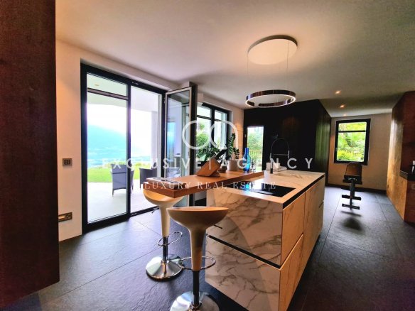 Modern kitchen with marble island, white bar stools, and glass doors opening to a patio and view.