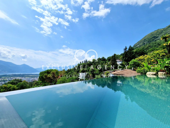 Infinity pool with turquoise water reflecting a blue sky, overlooking green hills and a hillside villa village.