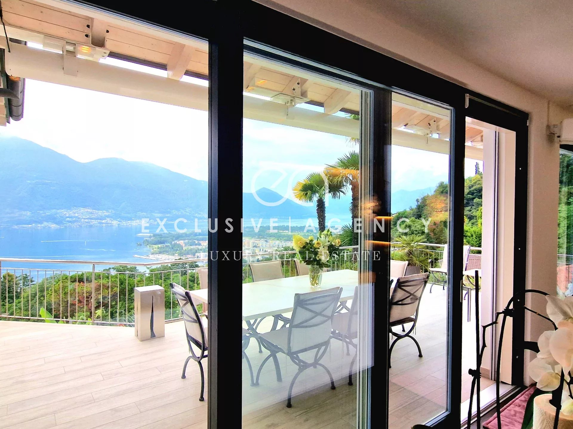 Luxurious balcony dining area with glass sliding doors opening to a scenic lake and mountain view.