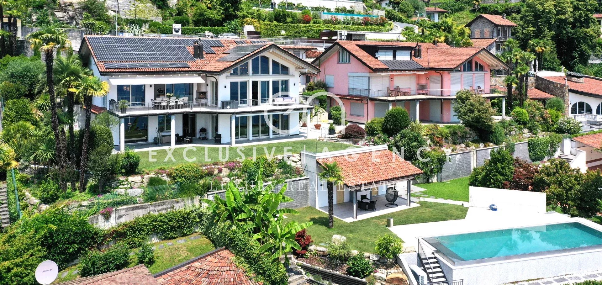 Luxurious hillside villas with red-tiled roofs, glass terraces, and a rectangular pool in the foreground, surrounded by lush greenery.