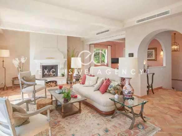 Luxurious living room with cream sofas and white armchairs around a wooden coffee table, facing a large white fireplace and terracotta tile floor.