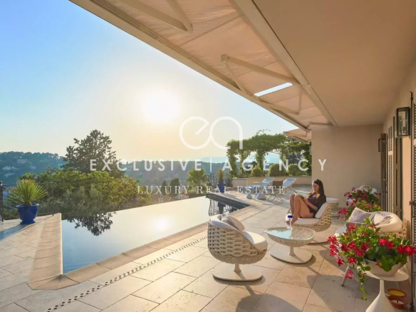 Luxurious outdoor terrace with an infinity pool, white wicker seating, and a woman relaxing in the sun overlooking hills at sunset.