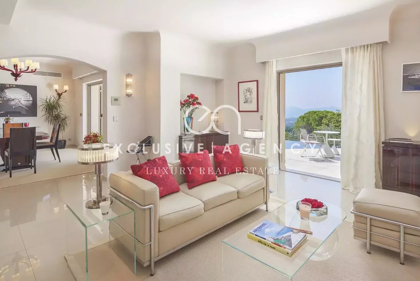 Bright living room with white sofa and red cushions, glass coffee table, and a balcony with hillside view
