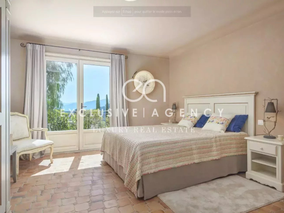 Bright bedroom with a large glass door opening to greenery, white bed frame, and neutral decor.