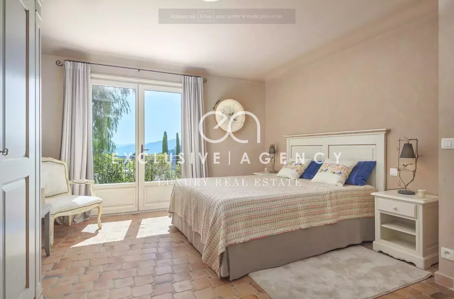 Bright bedroom with a large glass door opening to greenery, white bed frame, and neutral decor.